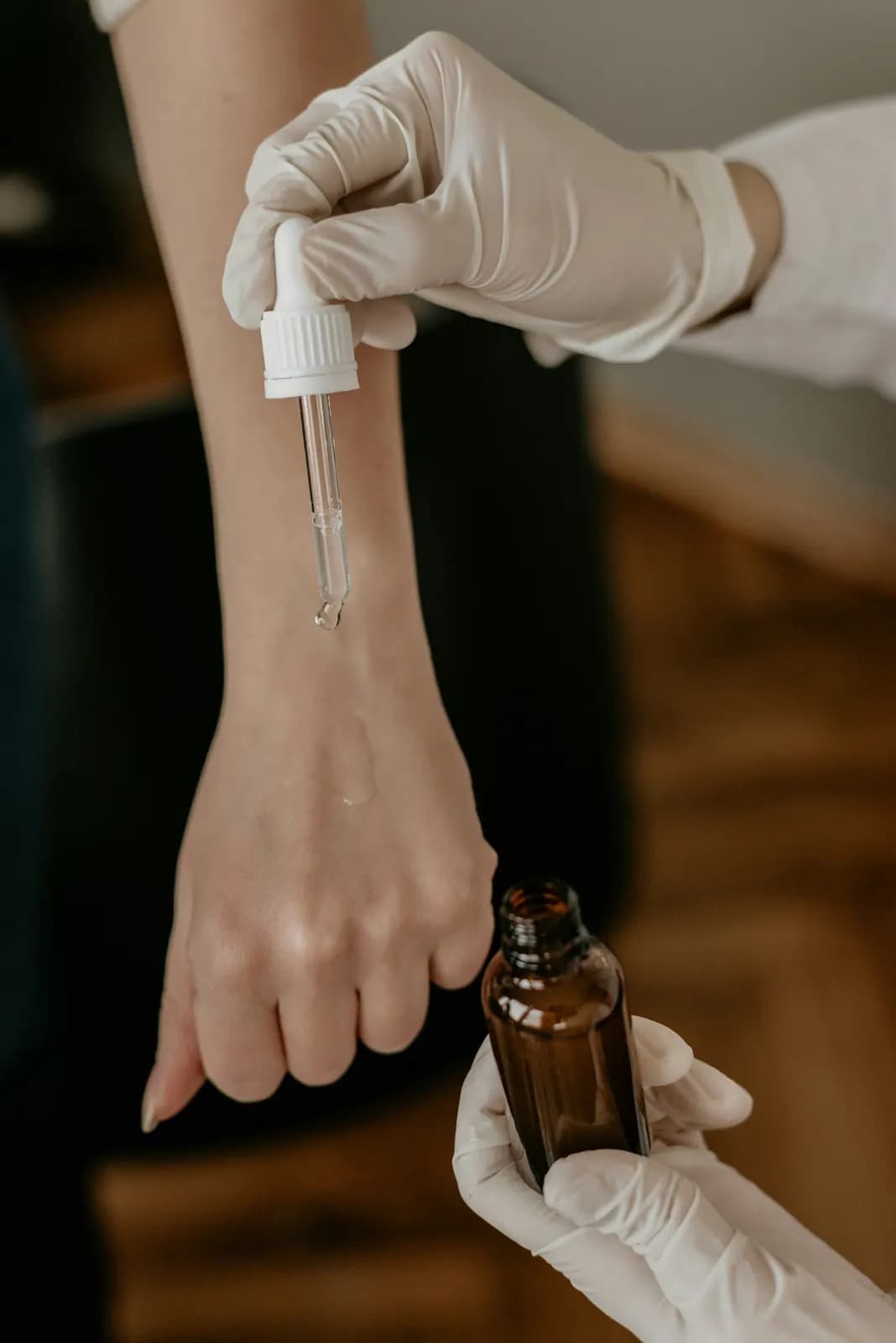 Des mains gantées déposent une goutte de sérum sur un poignet