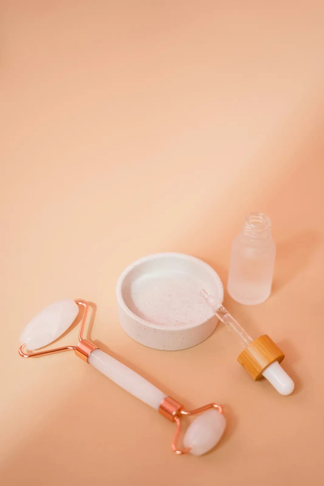 Rouleau de quartz rose et pipette sur fond pêche