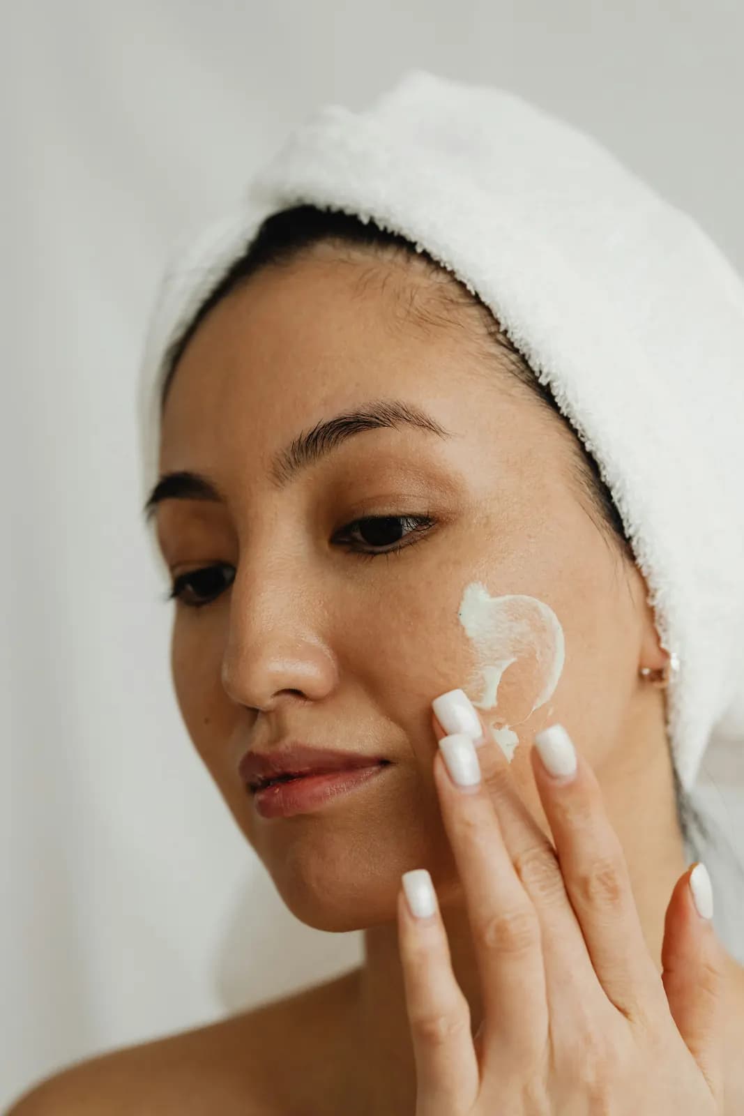 Une femme applique une crème sur sa joue, une serviette dans les cheveux